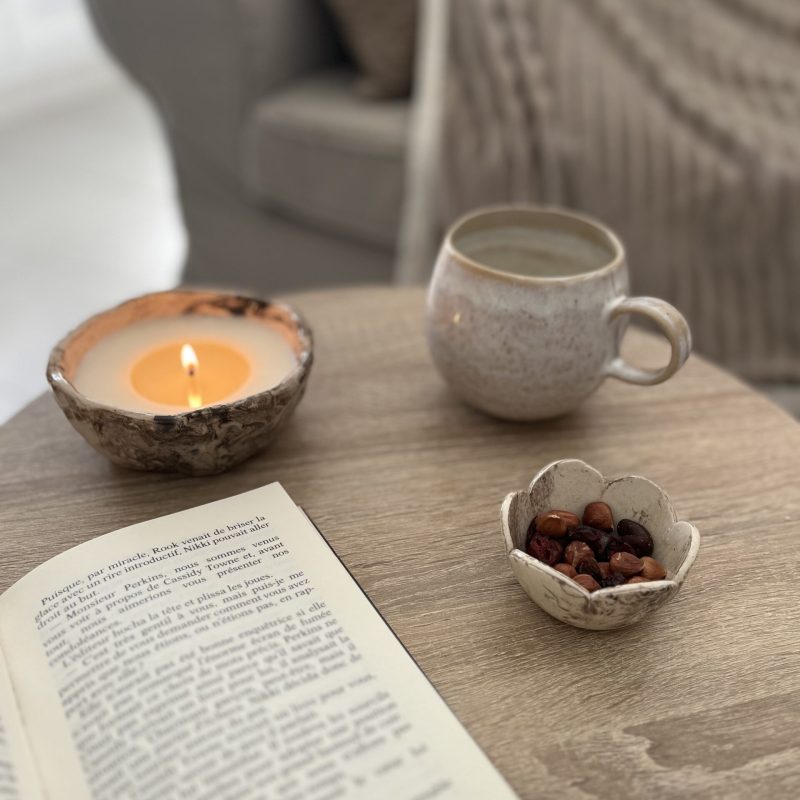 une bougie straciattella allumée, un mug et un livre ouvert sur une table basse
