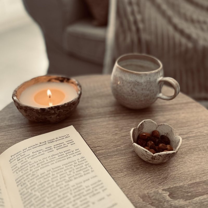 une bougie, un livre ouvert et un mug sur une table basse près d'une canapé