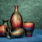 5 vases de poterie posées sur un drap bleu et le mur du fond est vert