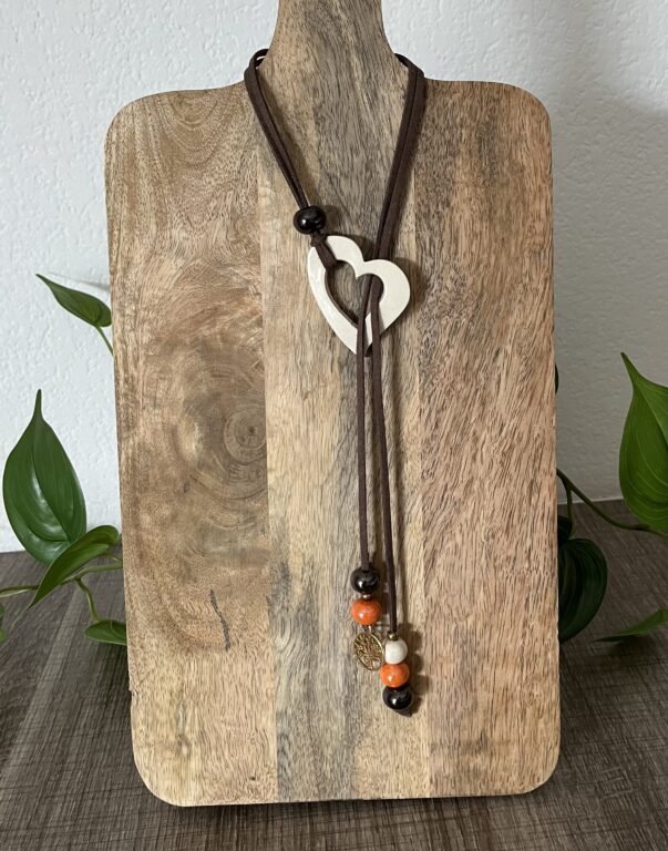 Sautoir avec un coeur en céramique, 6 perles en céramique (noir, orange, écru) et 1 breloque dorée sur un long cordon en suédine couleur taupe