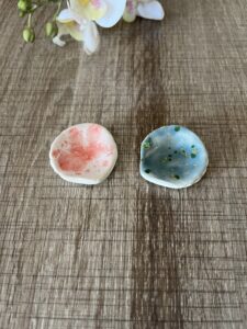 2 Coquillages en céramique : 1 de couleur rose et blanc et 1 de couleurs vert et bleu posés sur un plan de travail marron